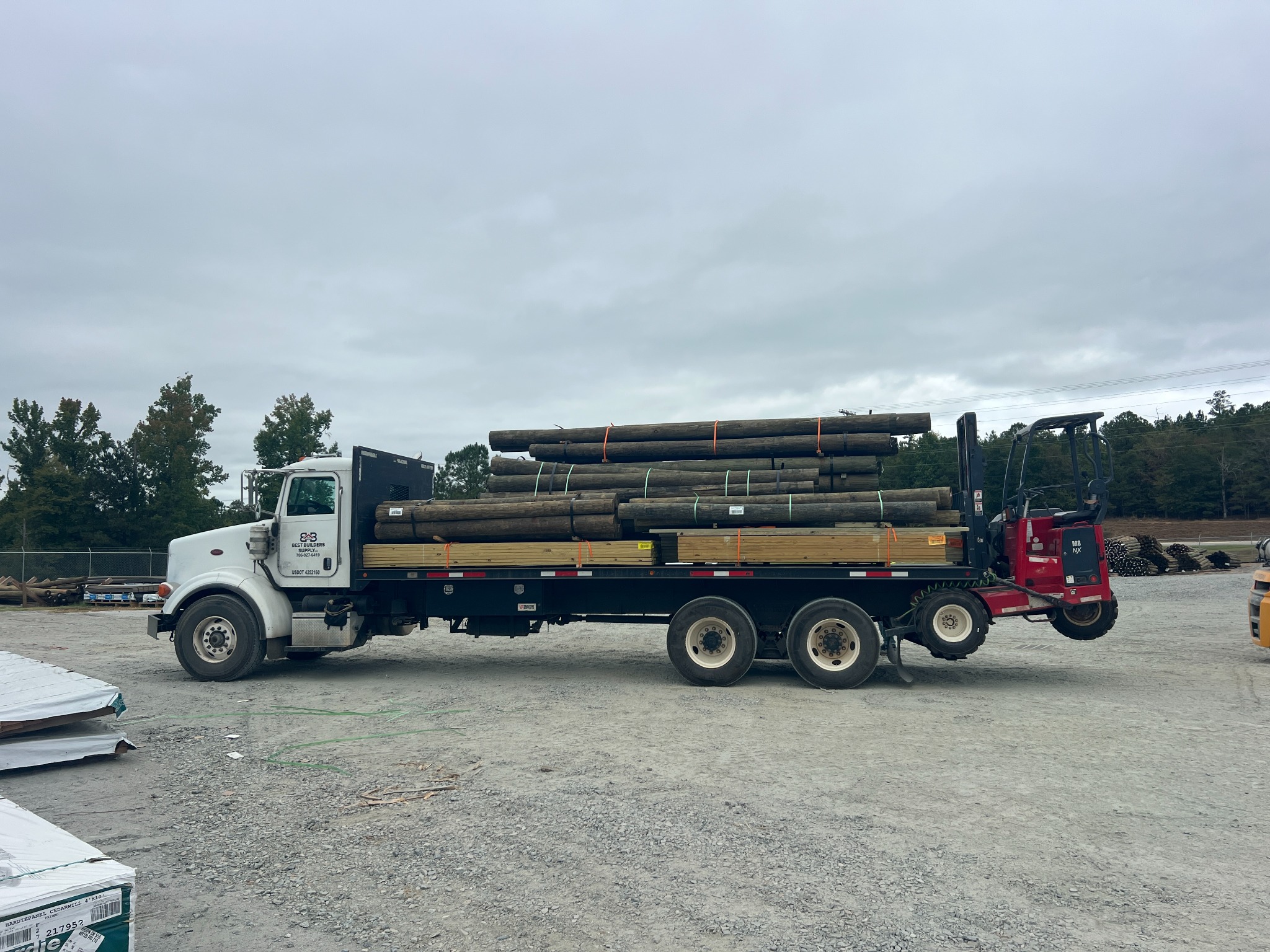 Side view of a Best Builders Supply truck carrying lumber and poles