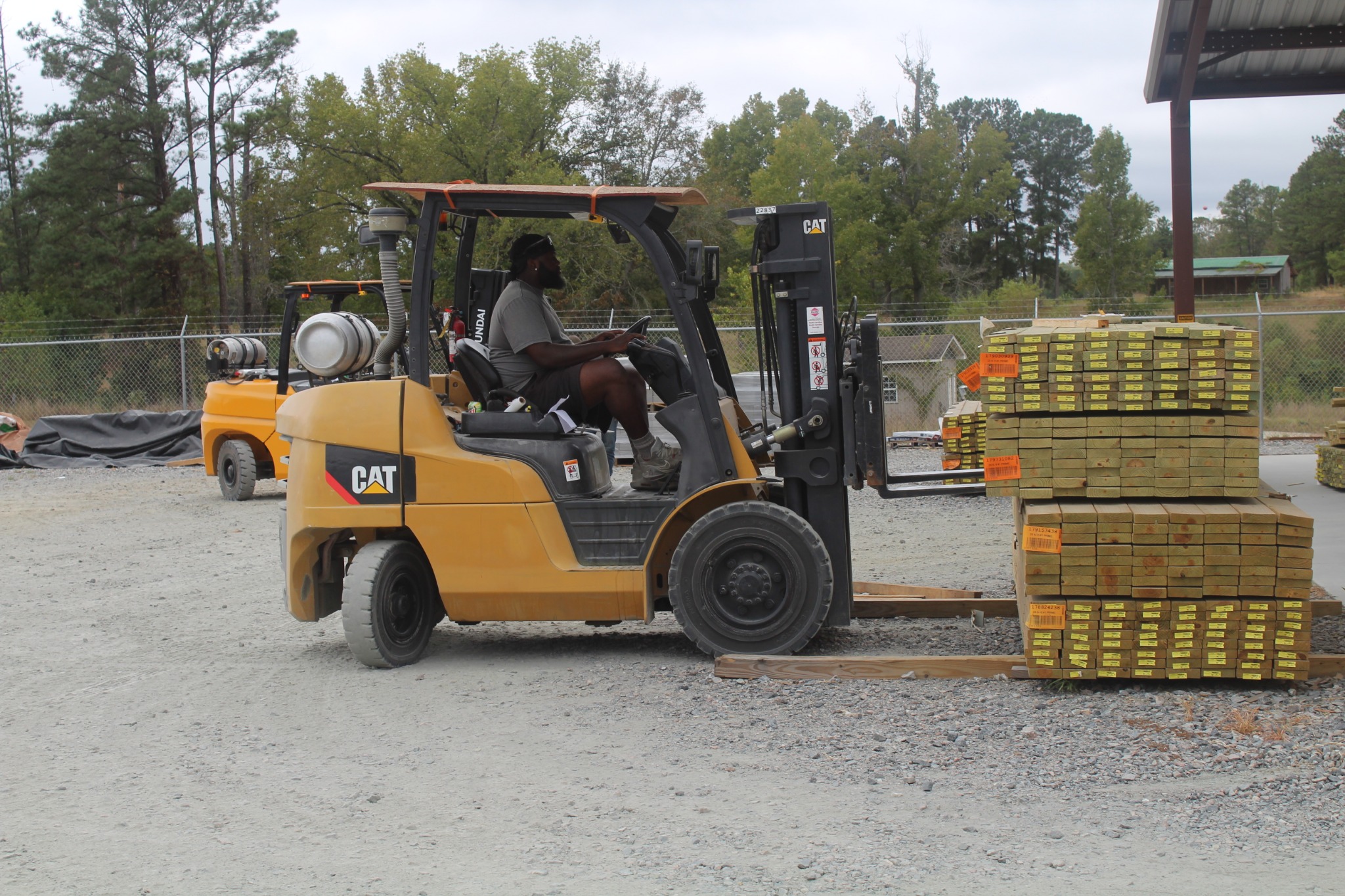 Team member operating a CAT forklift with bundled lumber in the yard